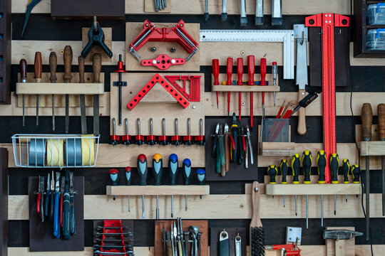Organized workshop tool wall with hand tools on french cleat system. Full frame view of a tidy wooden pegboard wall with neatly arranged screwdrivers pliers clamps and chisels in garage workshop