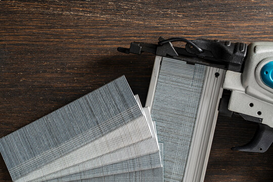 Brad nailer gun with collated brad nails on wooden background, closeup. Top view of a pneumatic brad nailer with blocks of steel finish nails on a dark wooden table in a carpentry workshop