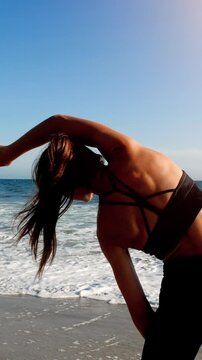 Athletic woman at the beach stretching and relaxing after her workout. Vertical video.