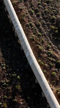 Aerial shot of the Los Angeles Aqueduct as it passes over some low mountains in California. The aqueduct supplies water to Los Angeles and Southern California. Vertical video.