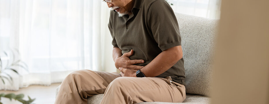 Abdominal pain stomach ache senior man stomach pain belly pain healthcare digestive problem home living room sofa Senior man sitting sofa living room holding abdomen with abdominal pain