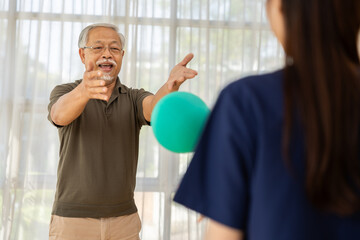 Fototapeta premium Senior man physical therapy exercise rehabilitation caregiver medicine elderly man reaching for green ball during physical therapy session with female caregiver bright clinic, recovery training