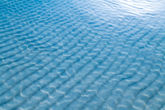 Beach sand ripples, sunlight and crystal clear shallow water.