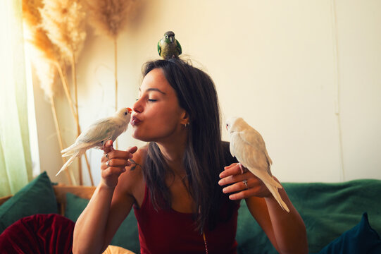 Young woman playing with her pet parakeets at home