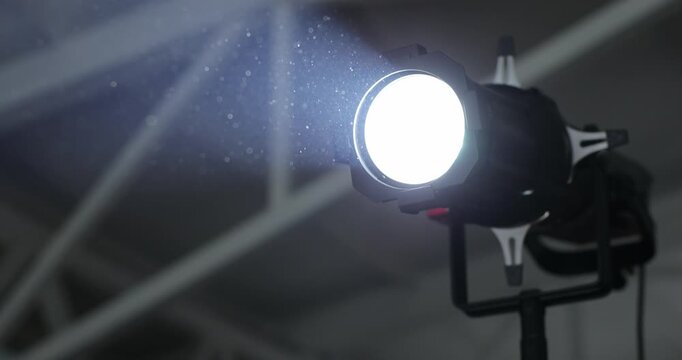 Cinematic close-up of bright professional stage spotlight shining powerful beam in dark event venue or studio with visible dust particles in light. Perfect for event, concert, and production content.