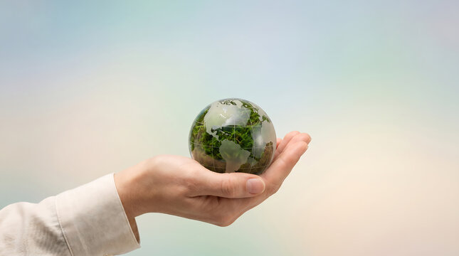 hand gently holding tiny Earth globe against soft pastel gradient background