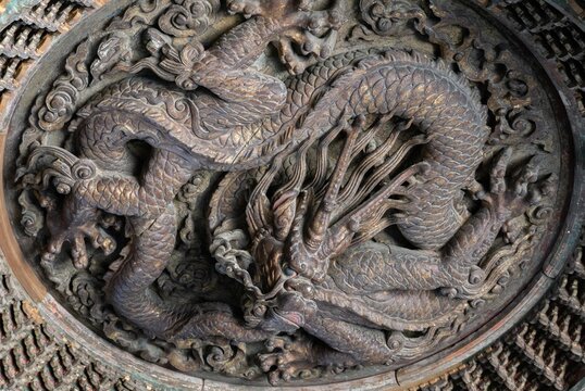 A close-up of an ancient Chinese wooden caisson ceiling carved in the shape of a Chinese dragon.
