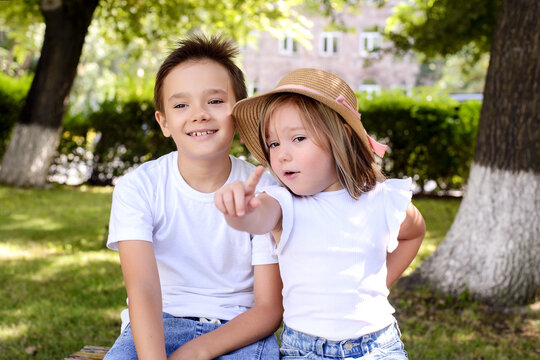 Happy brother and sister sitting together in a sunny park, pointing at something interesting. Family bonding, friendship, curiosity, and carefree childhood outdoors