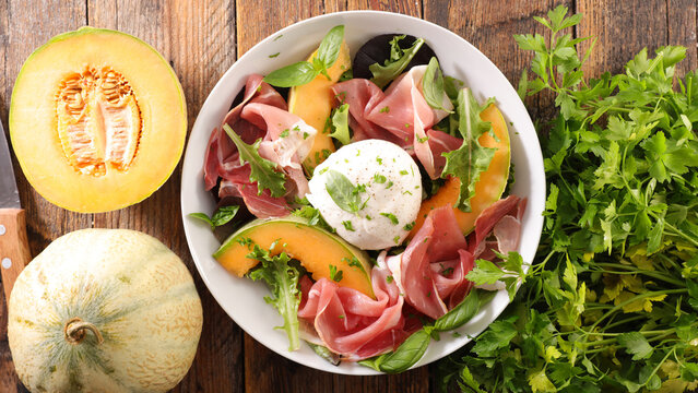 melon prosciutto burrata salad on wooden background
