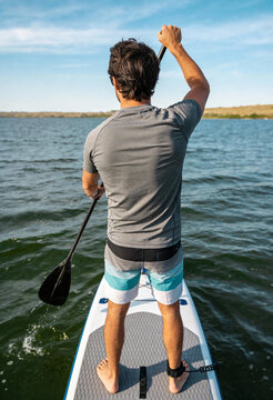 Mann von hinten beim Stand-Up-Paddling (SUP) auf einem ruhigen See an einem sonnigen Tag