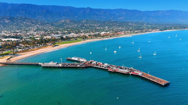 Stearns Wharf and white yachts on the blue waterscape. Drone footage over marina of Santa Barbara County, California on sunny day.