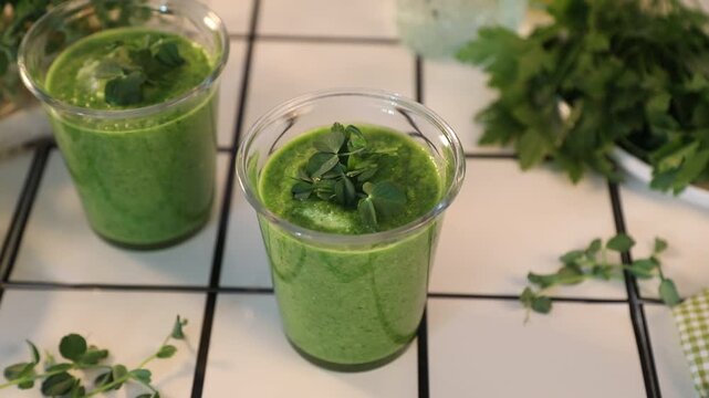 Fresh green gazpacho or smoothie in a glass with herbs microgreens in glass cups on a light background
