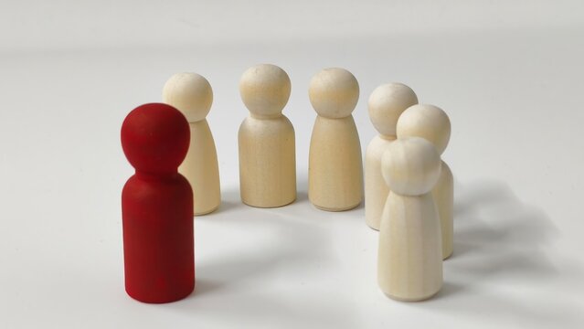 ​Leadership and influence concept with a red wooden figurine standing out in front of a group of white figurines on a plain background.