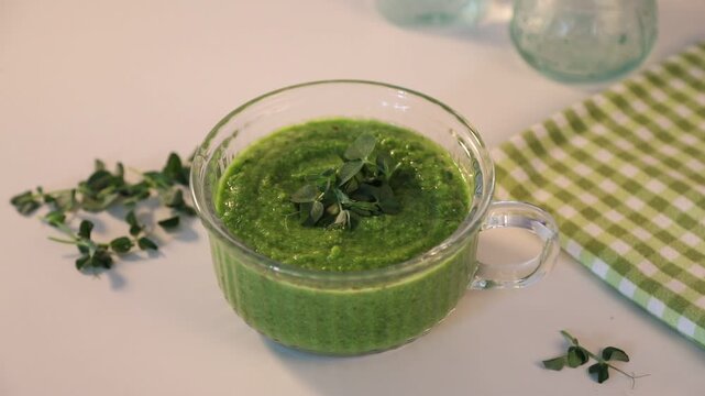 Fresh green gazpacho or smoothie in a glass with herbs microgreens in glass cups on a light background