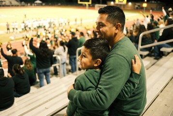 Fototapeta premium Father and son cheering together at a football game in a crowded stadium, enjoying family sports event 