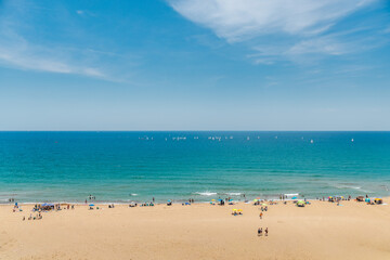 Fototapeta premium Young tourists relaxing on sandy beach of Mediterranean coast in Spain, colorful umbrellas, swimmers and sailboats on turquoise sea