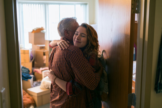 Father hugging his teenage daughter in a dorm room during move-in day, representing family support, college transition, student independence and emotional back-to-school moments