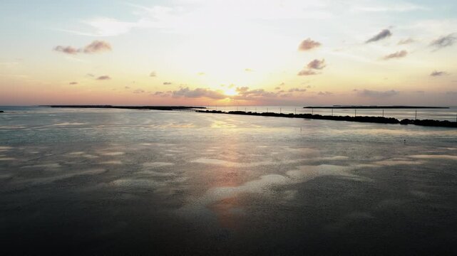 Cinematic forward drone push over calm tropical water during sunset in Islamorada, Florida Keys featuring golden reflections, island coastline, and peaceful ocean scenery.