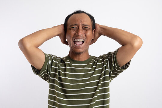 Asian man holding his head as an expression of headache with additional screaming as a sign of how painful it is.
