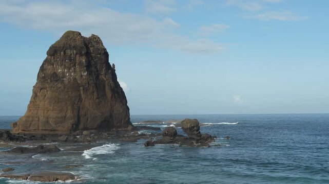 Majestic rocky sea stack standing tall in the blue ocean with waves crashing against the shore under a clear sunny sky with copy space.