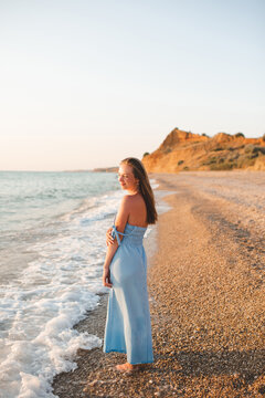 Young adult woman 30-35 year old wearing blue dress standing in water at beach over sea at background. Summer vacation time. 30s. Relaxation.