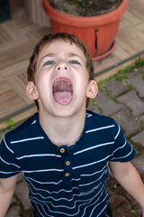 Little boy with head tilted back and wide open mouth catching rain outdoors, playful child lifestyle concept © Татьяна Швец