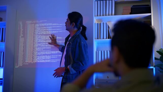 Male software developer presenting programming code projected on wall to audience in modern dark office. Tech talk, code walkthrough, bootcamp, mentorship, hackathon presentation, training session.