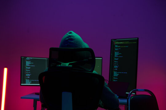 Hacker in Hoodie Working at Dual Monitors in Dark Neon Room