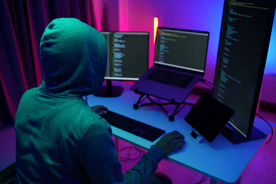 Hacker in Hoodie Working at Multi-Monitor Coding Setup