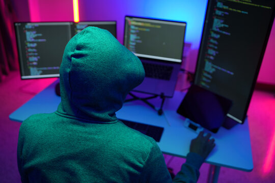Hacker in Hoodie Coding on Multiple Monitors in Neon Light