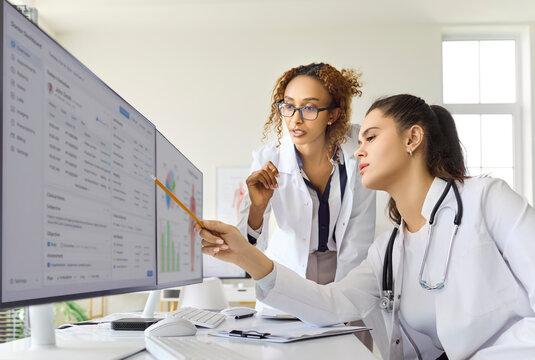 Doctors consultation at computer with medical records analysis. Physicians study charts on a widescreen monitor for diagnosis in a modern healthcare clinic. Clear clinic teamwork and analysis.