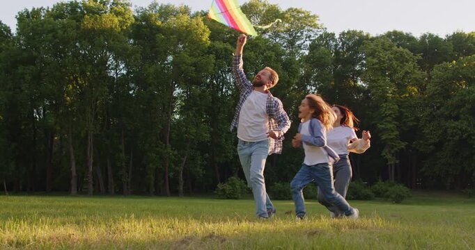 Happy family enjoying time together in nature while launching colorful kite into air. Joyful parents and child running together on sunny field, laughing and having fun during outdoor activity