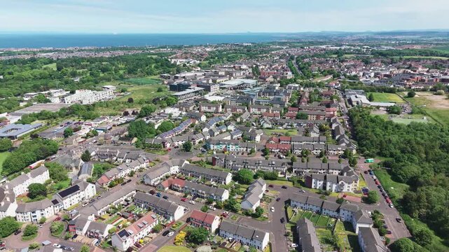 Cinematic aerial drone forward flight over Greendykes and Niddrie residential areas in Edinburgh, Scotland. Beautiful suburban cityscape stretching to the sea coast on a sunny summer day.