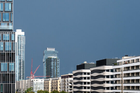 Dark blue sky hangs over urban skyline, apartments and highrise towers, where construction cranes mark downtown development beyond facades