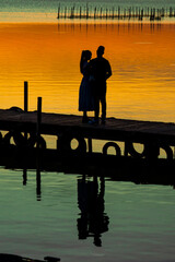 Obraz premium honeymoon. vacation. silhouette of a couple in love on a wooden pier, enjoying a sunset on a lake