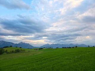 Obraz premium germany, sweeping alpine panorama with glowing clouds above verdant fields and majestic mountain chain
