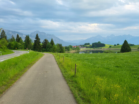 germany, charming hiking path and quiet bike route beside lake and alpine meadows beneath dramatic clouds