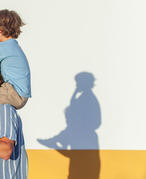Kind auf Schultern von Vater wirft Schatten an Hausmauer.