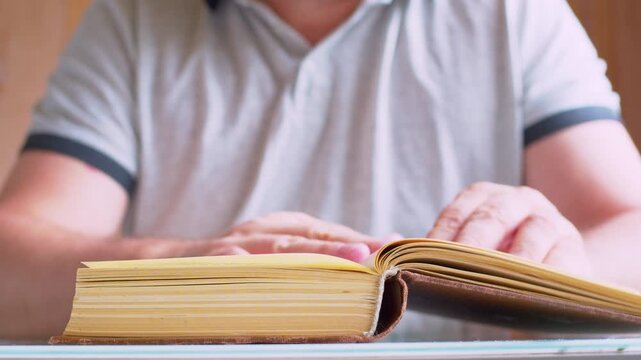 Cinematic macro shot of turning old book pages. Defocused man silhouette. Soft warm sunshine.