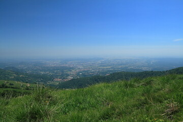 Fototapeta premium Panoramic view of a vast valley and distant plain from a green mountain hill under a clear blue sky
