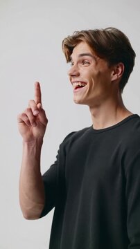 Young man in black t-shirt thinking and gesturing against light gray studio background, medium shot