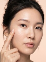 Obraz premium Young Asian woman applying clear gel serum to cheek for skin care
