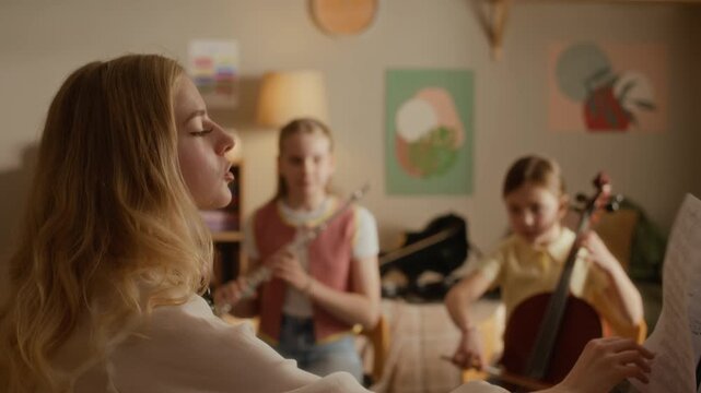 Zoom out shot of Caucasian teacher playing violin while guiding teenager playing flute and child playing cello during home music lesson. Footage ideal for promoting private tutoring
