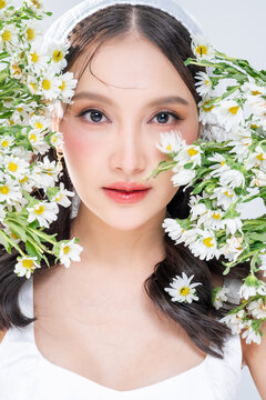 Extreme close up of Asian woman face framing with daisy flowers for botanical cosmetics skincare marketing campaign organic treatment concept holistic beauty wellness softness editorial