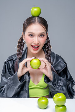 Playful Asian woman in leather jacket with green apples for creative nutrition diet marketing campaign street fashion aesthetic healthy lifestyle pop culture dynamic portrait studio