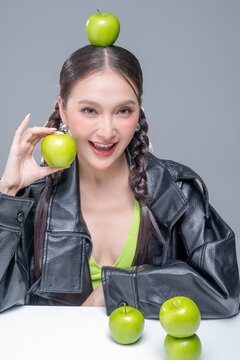 Playful Asian woman in leather jacket with green apples for creative nutrition diet marketing campaign street fashion aesthetic healthy lifestyle pop culture dynamic portrait