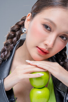 Confident Asian woman balancing tower of green apples for creative nutrition diet marketing campaign neon street fashion aesthetic healthy lifestyle conceptual portrait studio