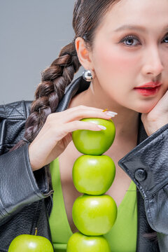 Confident Asian woman balancing tower of green apples for creative nutrition diet marketing campaign neon street fashion aesthetic healthy lifestyle conceptual portrait studio