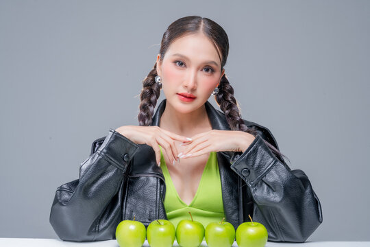 Confident Asian woman behind row of green apples for botanical cosmetics skincare marketing campaign neon street fashion aesthetic healthy lifestyle premium organic nutrition portrait stock