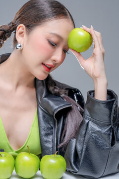 Intense Asian woman hiding face in leather jacket with green apples for creative cosmetics skincare marketing campaign edgy street fashion aesthetic healthy organic nutrition portrait